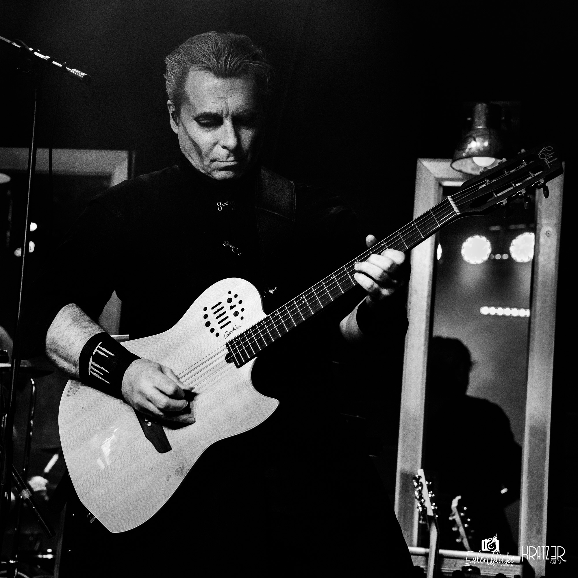 Schwarz-Weiß-Aufnahme eines Gitarristen, der auf der Bühne eine Akustikgitarre spielt.