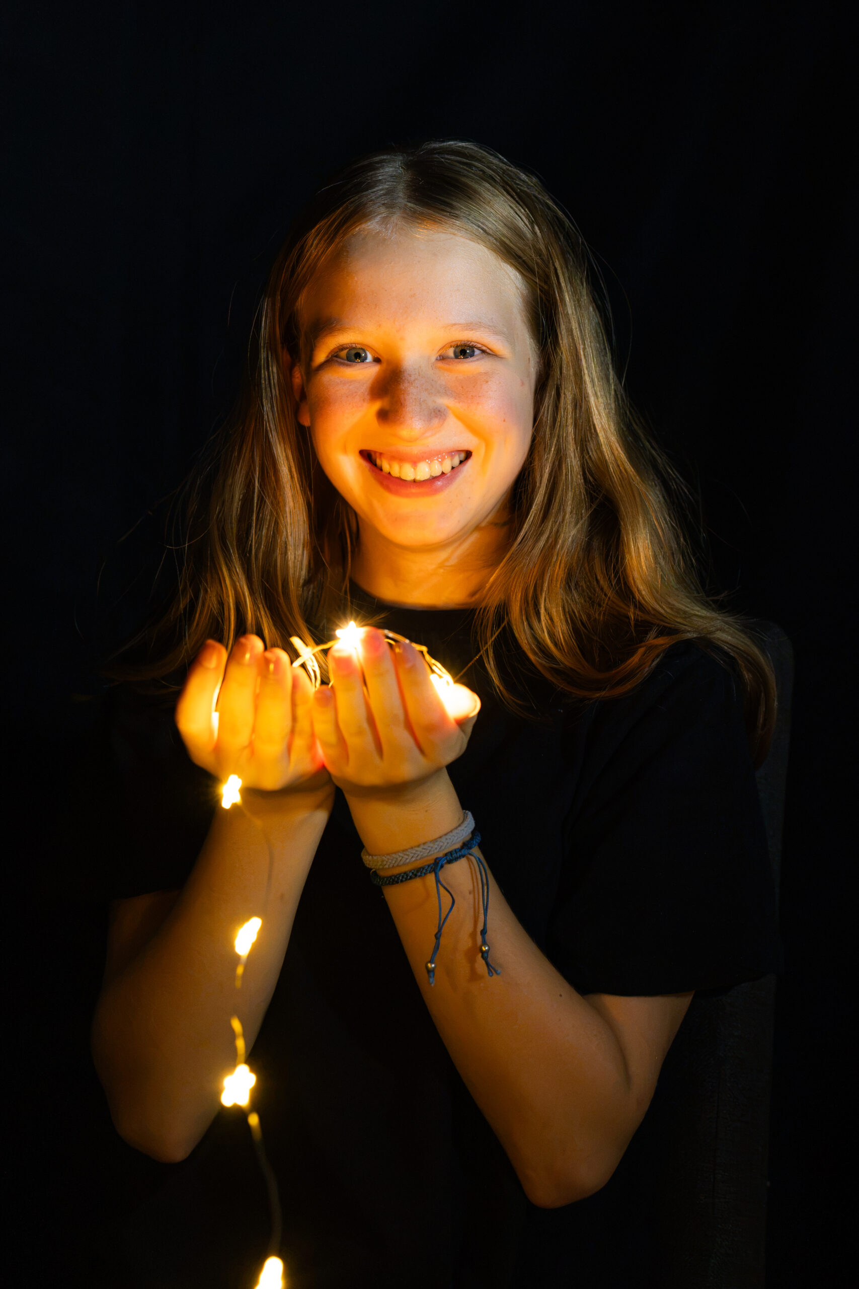 Lächelndes Mädchen hält eine leuchtende Lichterkette in beiden Händen, die ihr Gesicht warm beleuchtet.